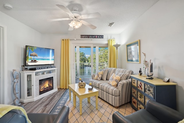 living room with a textured ceiling, ceiling fan, and light hardwood / wood-style floors