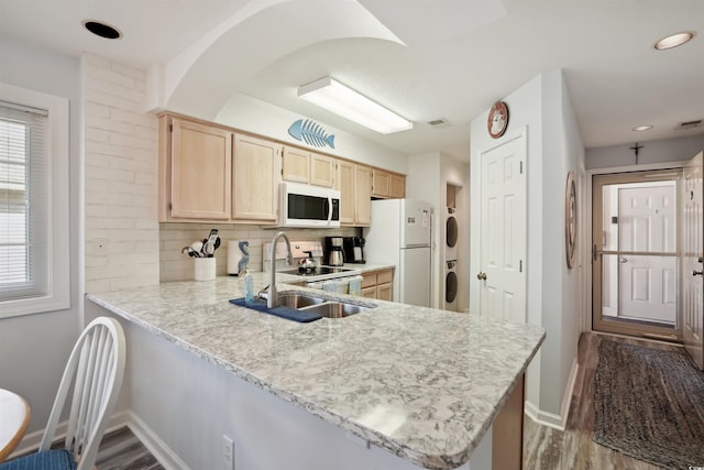 kitchen featuring white appliances, stacked washer / drying machine, kitchen peninsula, light brown cabinets, and tasteful backsplash