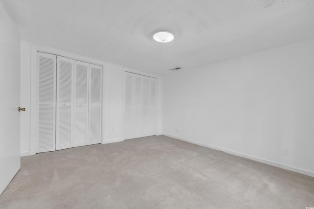 unfurnished bedroom with light colored carpet and multiple closets