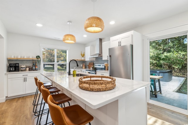 kitchen with wall chimney range hood, hanging light fixtures, sink, appliances with stainless steel finishes, and white cabinetry