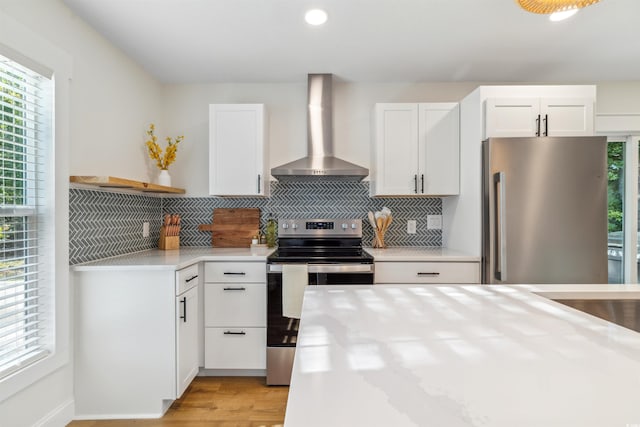 kitchen with white cabinets, stainless steel appliances, plenty of natural light, and wall chimney exhaust hood