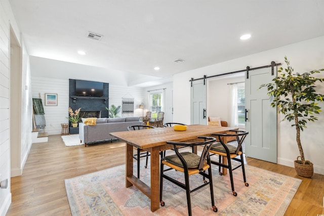 dining space with a barn door, light wood-type flooring, and a fireplace