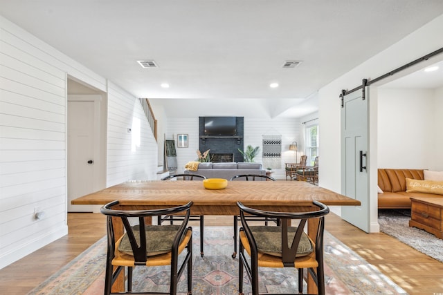 dining area featuring a barn door, light hardwood / wood-style floors, and wooden walls