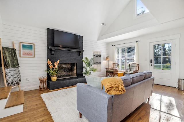 living room featuring wooden walls, a fireplace, high vaulted ceiling, and light wood-type flooring