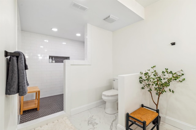 bathroom with a tile shower and toilet