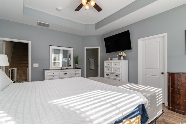 bedroom with light wood-type flooring, a raised ceiling, and ceiling fan