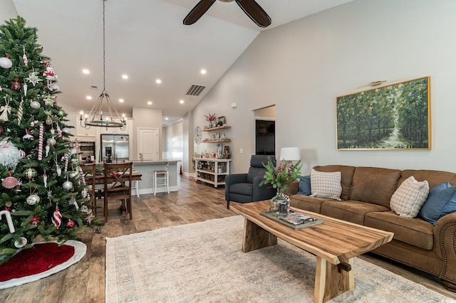 living room featuring high vaulted ceiling, wood-type flooring, and ceiling fan with notable chandelier