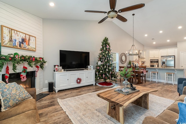 living room with a fireplace, ceiling fan with notable chandelier, hardwood / wood-style flooring, and high vaulted ceiling