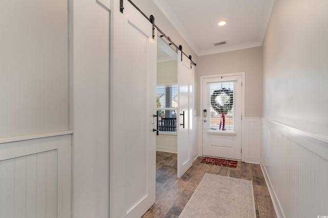 doorway with a barn door, crown molding, and dark wood-type flooring