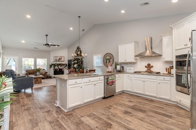 kitchen featuring ceiling fan, wall chimney exhaust hood, kitchen peninsula, pendant lighting, and light hardwood / wood-style floors