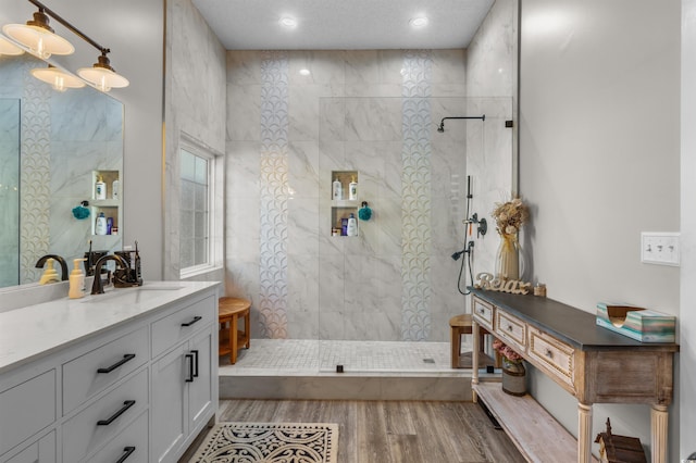 bathroom with a tile shower, hardwood / wood-style floors, vanity, and a textured ceiling