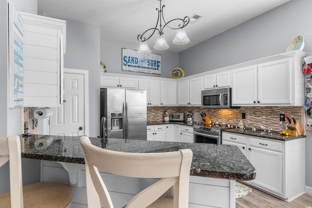 kitchen featuring a breakfast bar, dark stone counters, white cabinets, light wood-type flooring, and appliances with stainless steel finishes