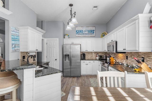 kitchen featuring kitchen peninsula, appliances with stainless steel finishes, a towering ceiling, sink, and pendant lighting