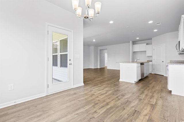 kitchen featuring decorative light fixtures, an island with sink, a notable chandelier, light hardwood / wood-style floors, and white cabinets