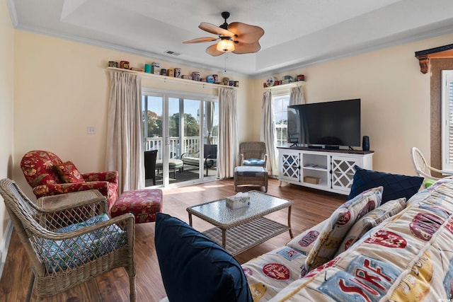 living room with a tray ceiling, ceiling fan, dark hardwood / wood-style flooring, and ornamental molding