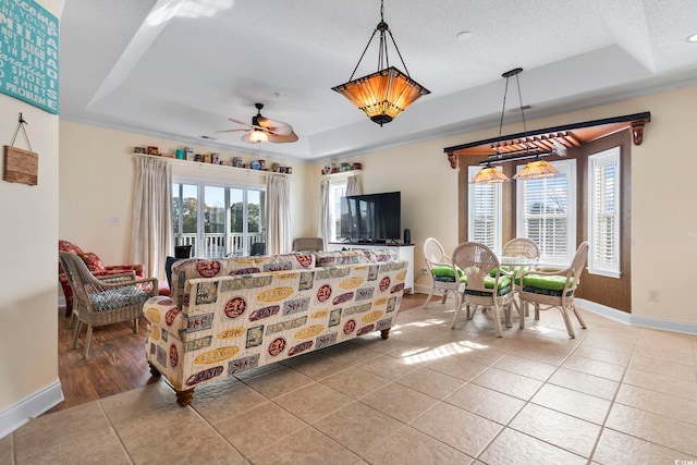 tiled living room with ceiling fan, a textured ceiling, and a tray ceiling