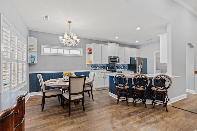 kitchen featuring white cabinets, wood-type flooring, stainless steel appliances, and hanging light fixtures