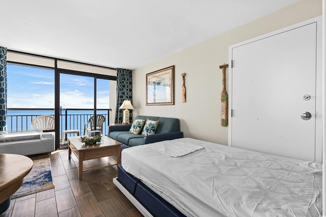 bedroom featuring access to exterior, dark hardwood / wood-style flooring, a water view, and a wall of windows