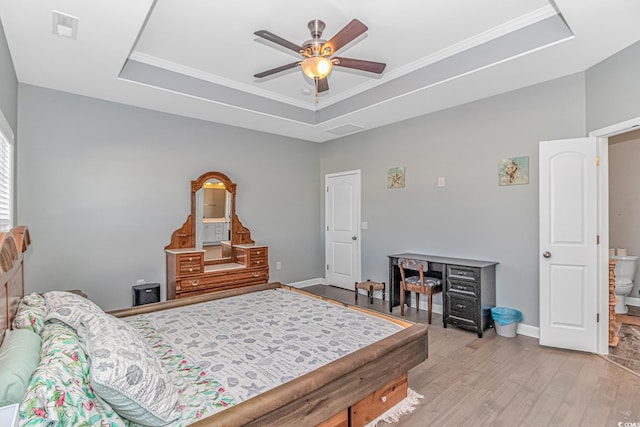 bedroom with ceiling fan, light hardwood / wood-style floors, a raised ceiling, and ensuite bath