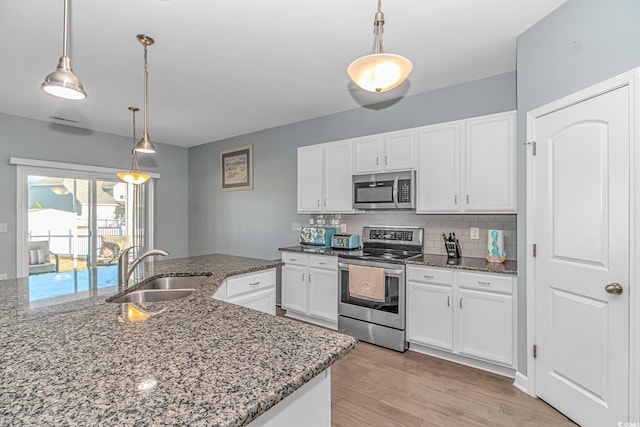 kitchen with white cabinetry, sink, dark stone counters, pendant lighting, and appliances with stainless steel finishes