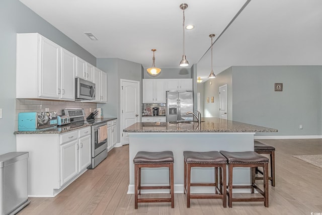 kitchen featuring backsplash, a center island with sink, hanging light fixtures, appliances with stainless steel finishes, and white cabinetry