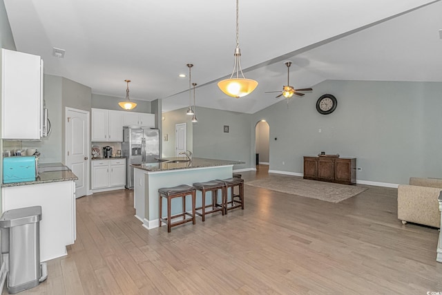 kitchen featuring white cabinetry, ceiling fan, stainless steel fridge with ice dispenser, dark stone countertops, and a kitchen island with sink