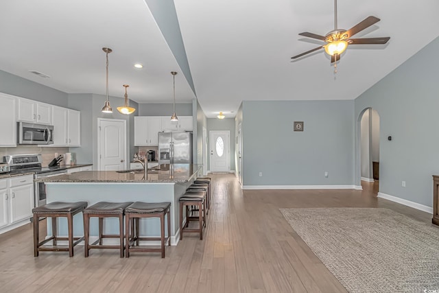 kitchen with a kitchen island with sink, dark stone countertops, appliances with stainless steel finishes, tasteful backsplash, and white cabinetry