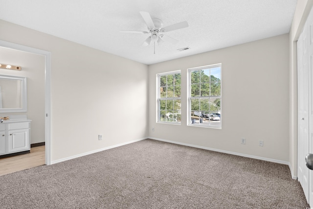 unfurnished bedroom featuring ensuite bath, light carpet, and ceiling fan