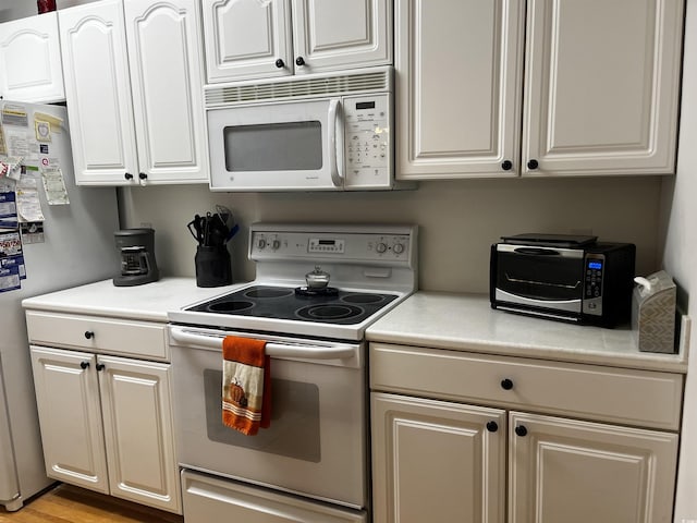 kitchen with white cabinets, light hardwood / wood-style floors, and white appliances