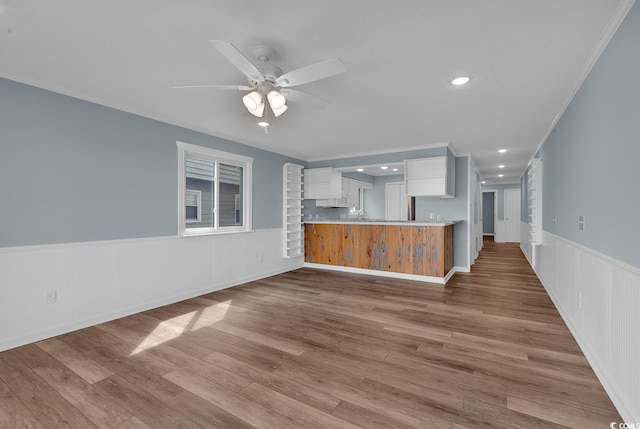 unfurnished living room with light wood-type flooring, ceiling fan, and ornamental molding