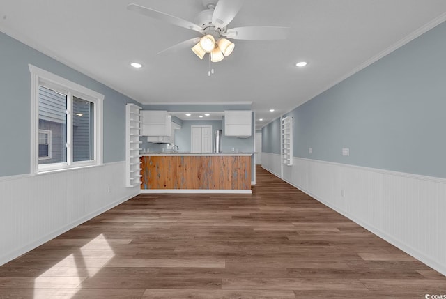 kitchen featuring kitchen peninsula, ceiling fan, crown molding, hardwood / wood-style flooring, and white cabinetry