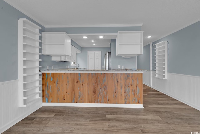 kitchen featuring kitchen peninsula, light stone counters, ornamental molding, hardwood / wood-style floors, and white cabinetry