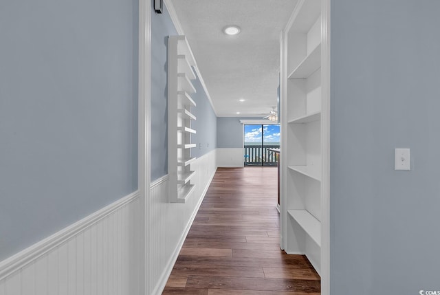 hallway with dark wood-type flooring, a textured ceiling, and ornamental molding