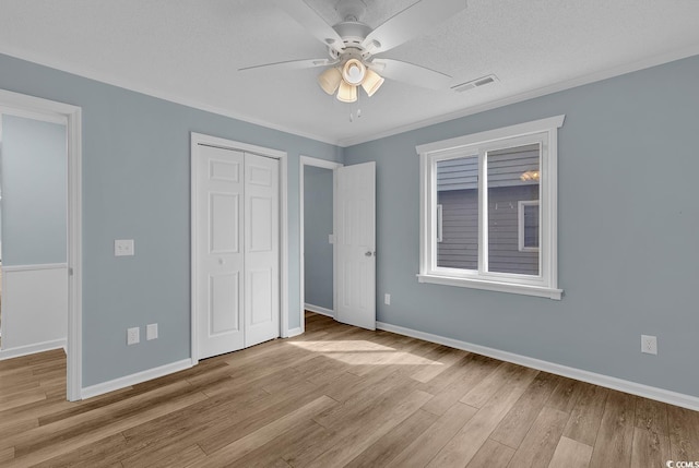 unfurnished bedroom featuring ceiling fan, ornamental molding, a textured ceiling, light hardwood / wood-style floors, and a closet