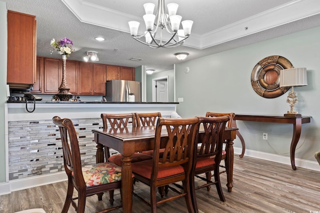 dining area featuring crown molding, wood-type flooring, a tray ceiling, and a textured ceiling