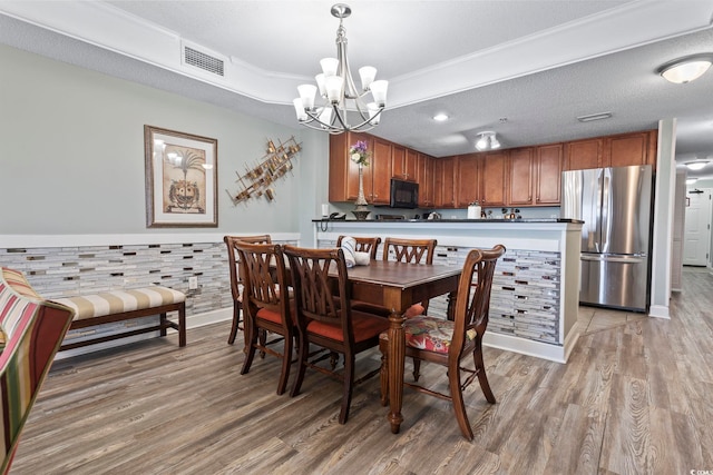 dining room with an inviting chandelier, wood-type flooring, ornamental molding, and a textured ceiling