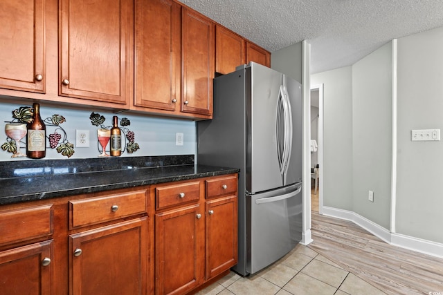 kitchen featuring dark stone countertops, light tile patterned floors, stainless steel refrigerator, and a textured ceiling