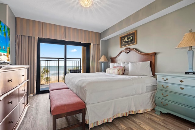 bedroom with access to exterior, wood-type flooring, and a water view