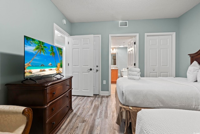 bedroom featuring light wood-type flooring, a textured ceiling, and ensuite bathroom