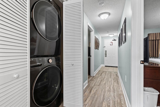 clothes washing area with stacked washer and clothes dryer, a textured ceiling, and light wood-type flooring