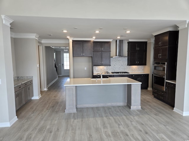 kitchen with decorative backsplash, light countertops, wall chimney range hood, gas cooktop, and a sink