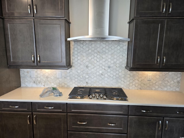 kitchen with stainless steel gas cooktop, light countertops, wall chimney range hood, dark brown cabinets, and decorative backsplash