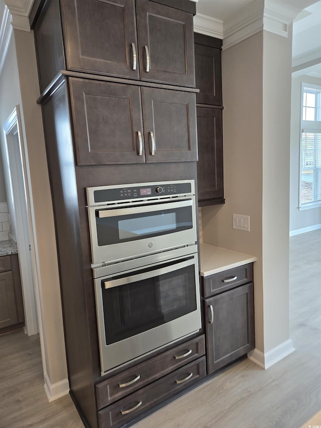 kitchen featuring double oven, light wood-type flooring, light countertops, and ornamental molding