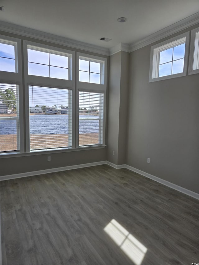 spare room with a water view, visible vents, baseboards, ornamental molding, and dark wood finished floors