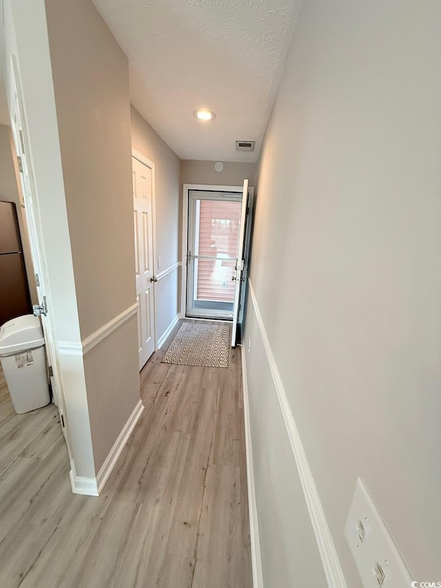 hall with light hardwood / wood-style flooring and a textured ceiling