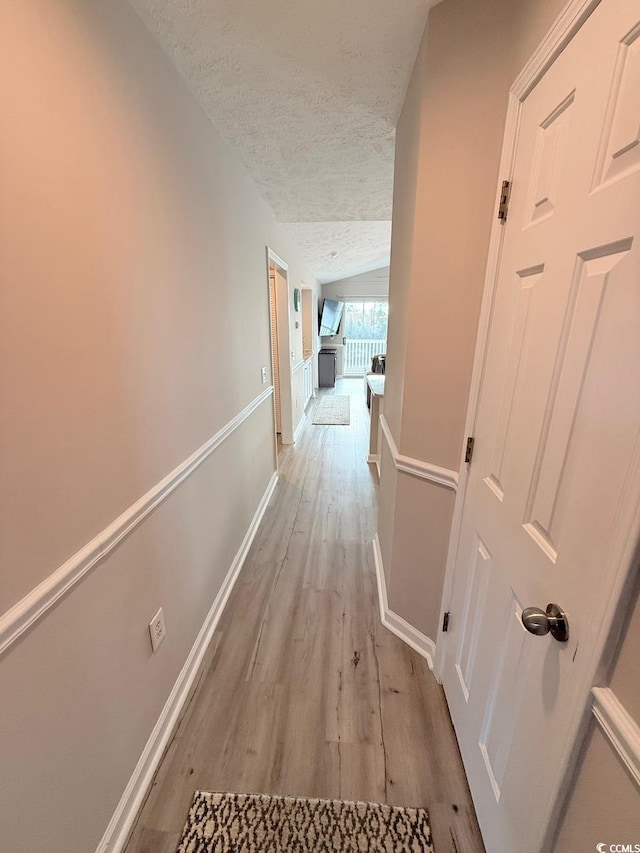 corridor featuring lofted ceiling, a textured ceiling, and light wood-type flooring