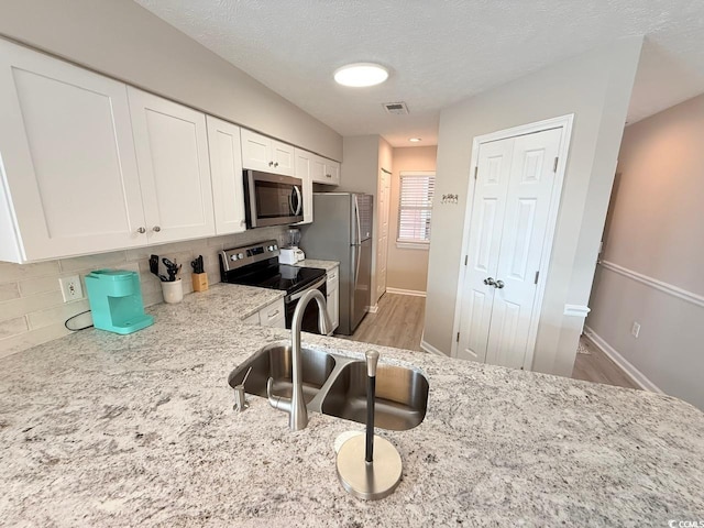 kitchen with backsplash, stainless steel appliances, light stone countertops, light hardwood / wood-style floors, and white cabinets