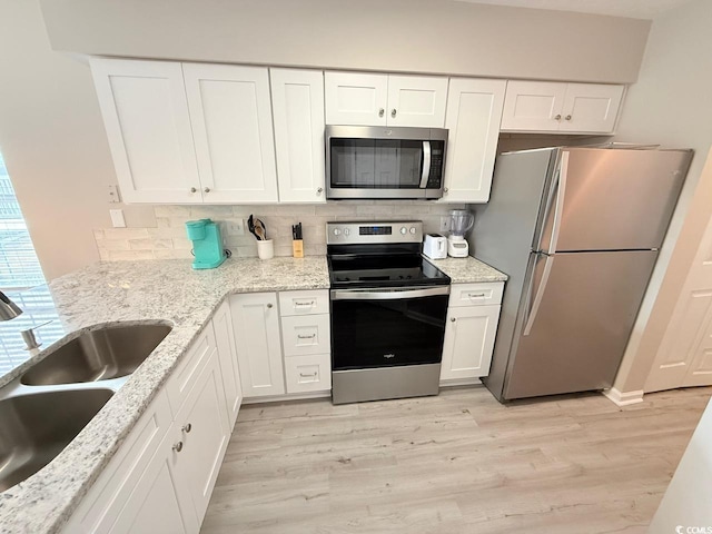 kitchen with stainless steel appliances, white cabinetry, sink, and light hardwood / wood-style flooring