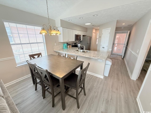 dining room featuring lofted ceiling, sink, a chandelier, light hardwood / wood-style floors, and a textured ceiling