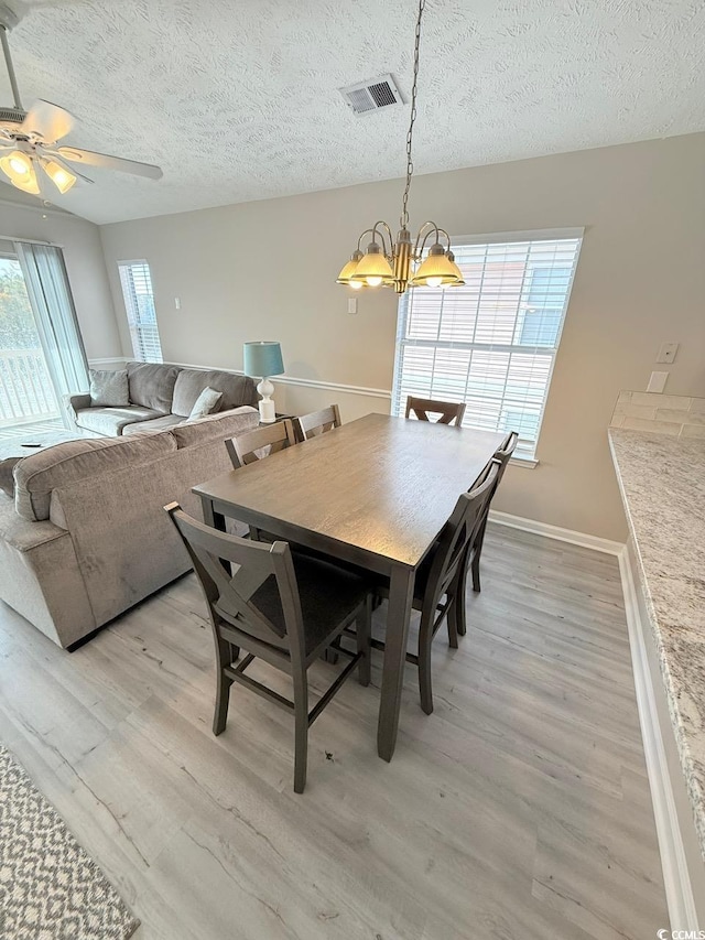 dining room with ceiling fan with notable chandelier, light hardwood / wood-style flooring, and a textured ceiling